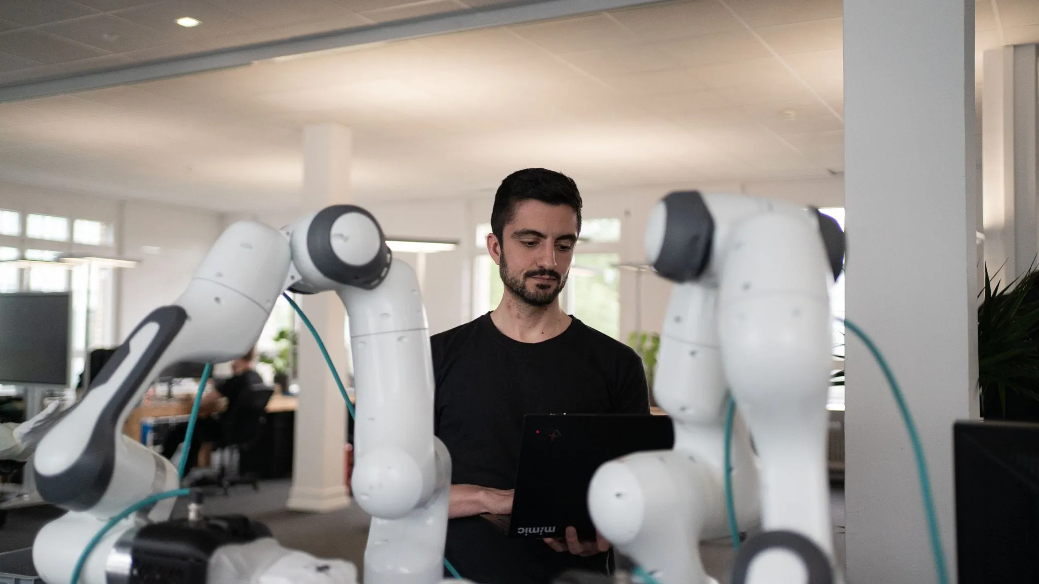 Mitarbeiter mit Laptop zwischen Roboterarmen